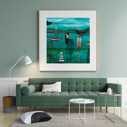 Art print by Kathryn Furniss. Blue tones with a mountain scape in the background while the forground features different waka paddles sticking out of the water with a bird perched on one and rock cairns below. Displayed in a wooden frame with white border on a soft grey wall above a light green couch and white coffee table and lamp.