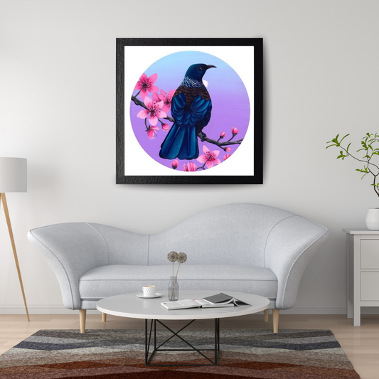 Living room setting in white colours with a feature print on the wall in a square black frame. The art print is a large blue Tui bird sitting on a flowering manuka branch with pink flowers.