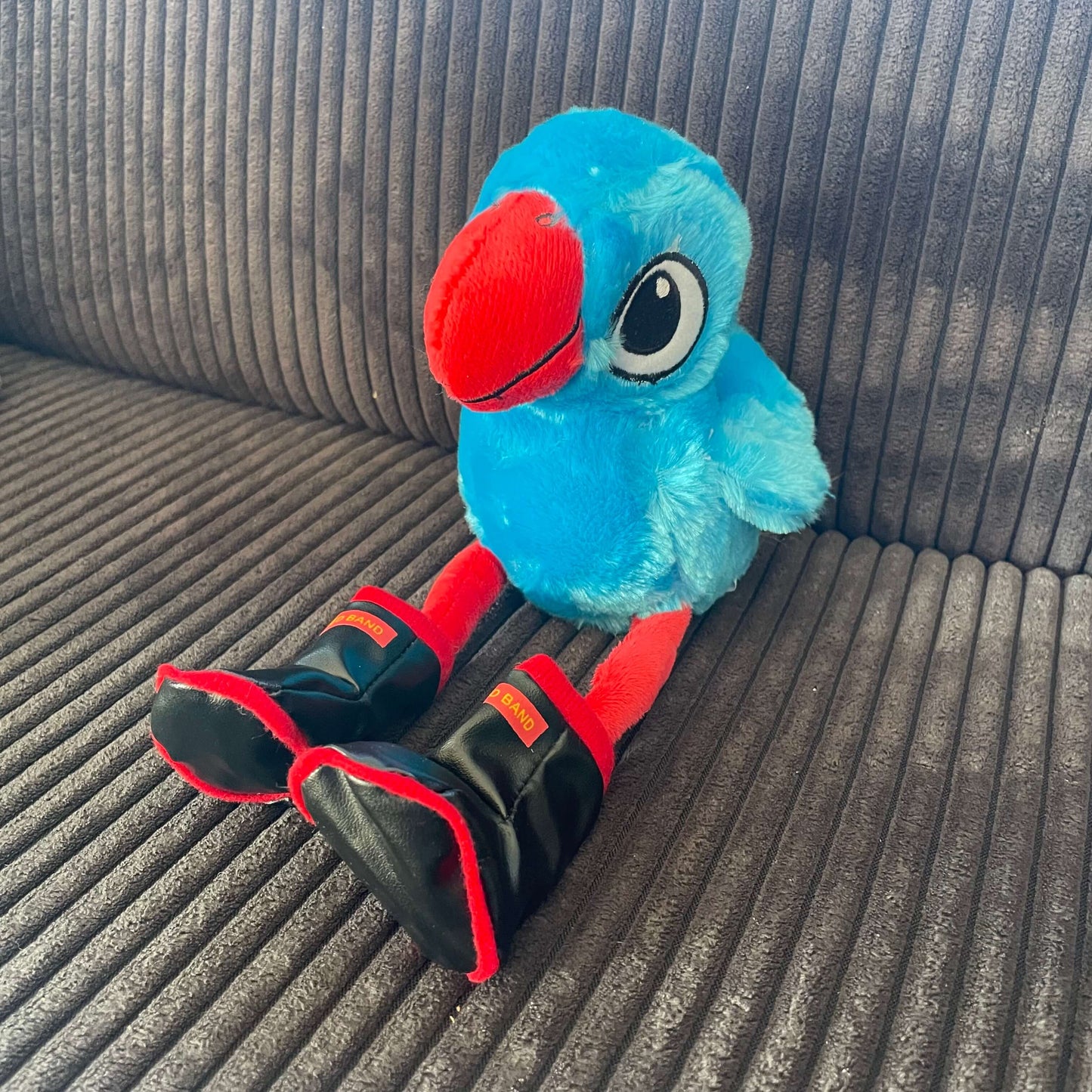 Plush pukeko toy wearing Redband gumboots sitting on a couch.