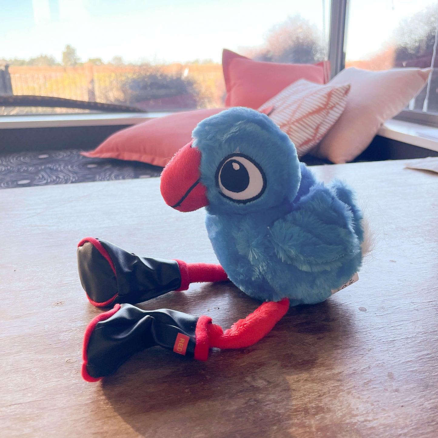 Plush pukeko toy wearing Redband gumboots sitting on a table with a widow seat in the background.