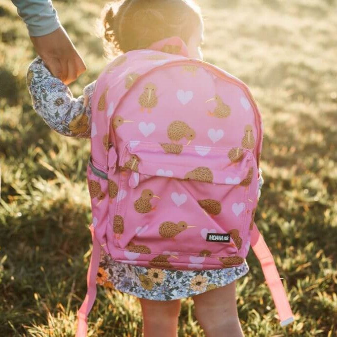 Young child wearing a pink kids backpack with lighter pink hearts and brown kiwi birds print.