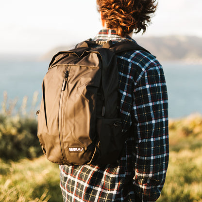 Man in plaid shirt overlooking the ocean and wearing a black Moana RD backpack.