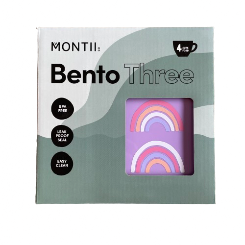 Front of a MontiiCo Bento Three lunchbox packaging with a glimpse to the purple lunchbox with rainbow print.