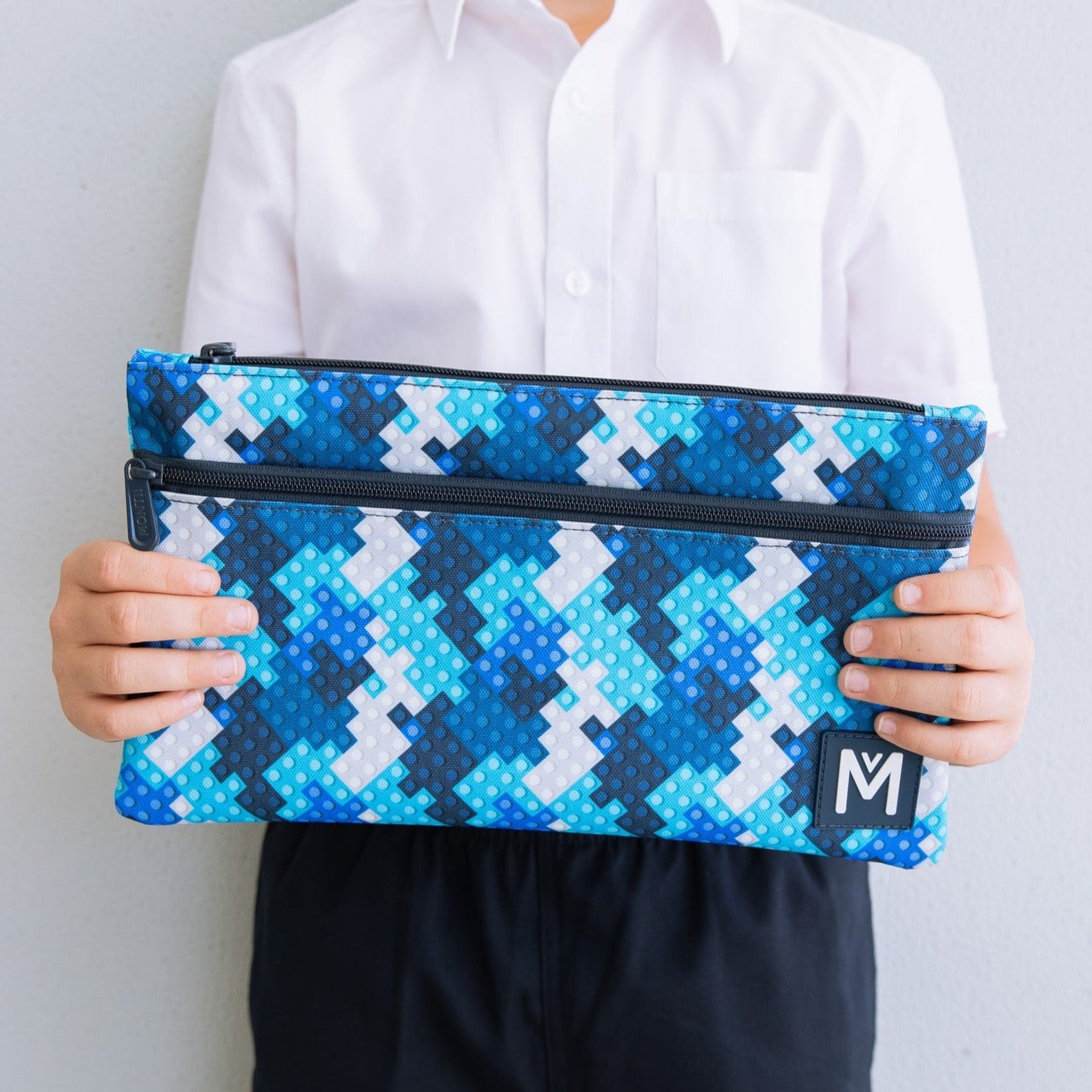 Childs hands holding a MontiiCo pencil case in a blue block print.