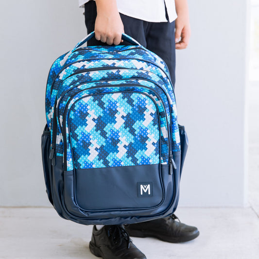 Childs hand holding the top handle of a backpack that is multi shades of blue with a block print.