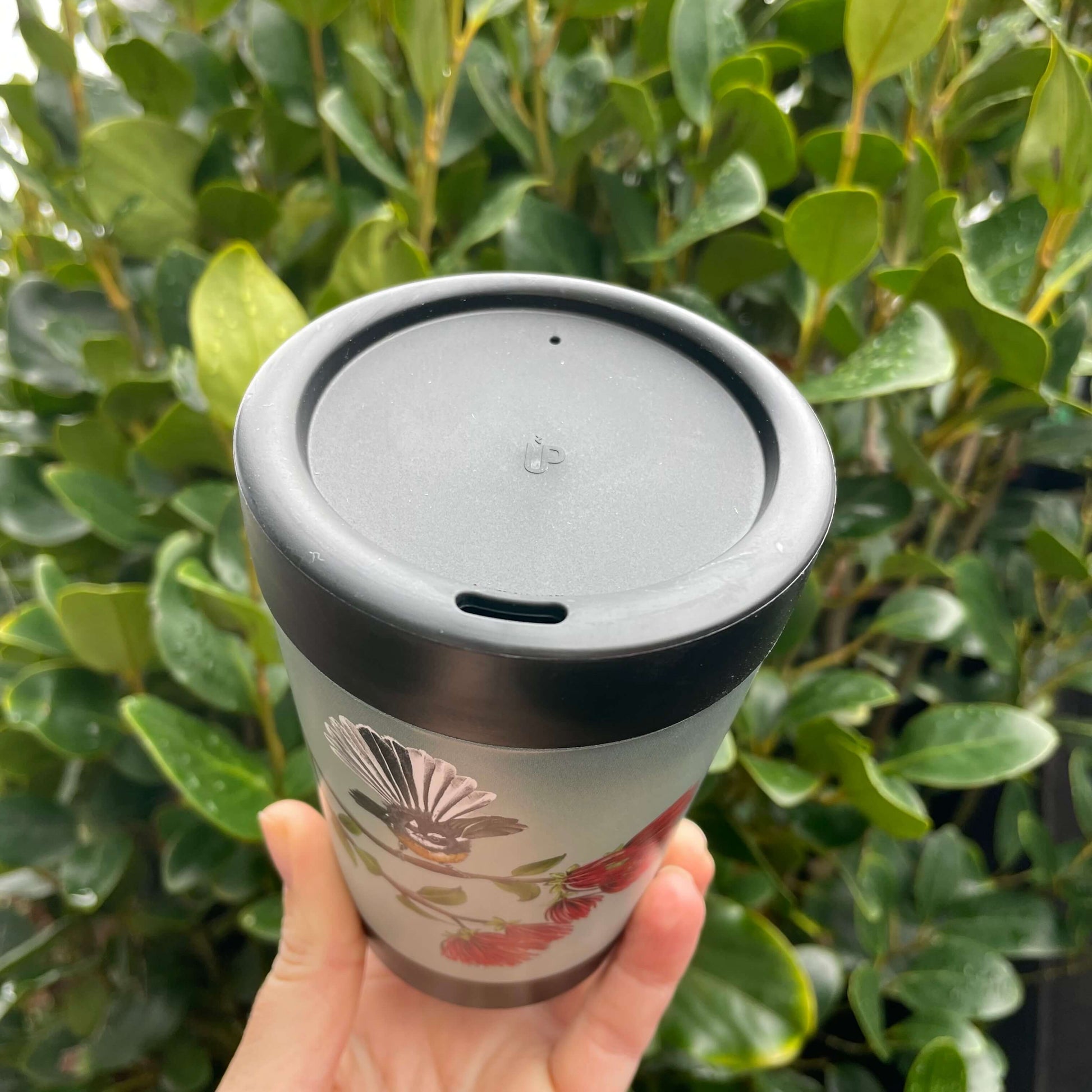 Birds eye view of a black reusable coffee cup with a peek at the fantail design on side.