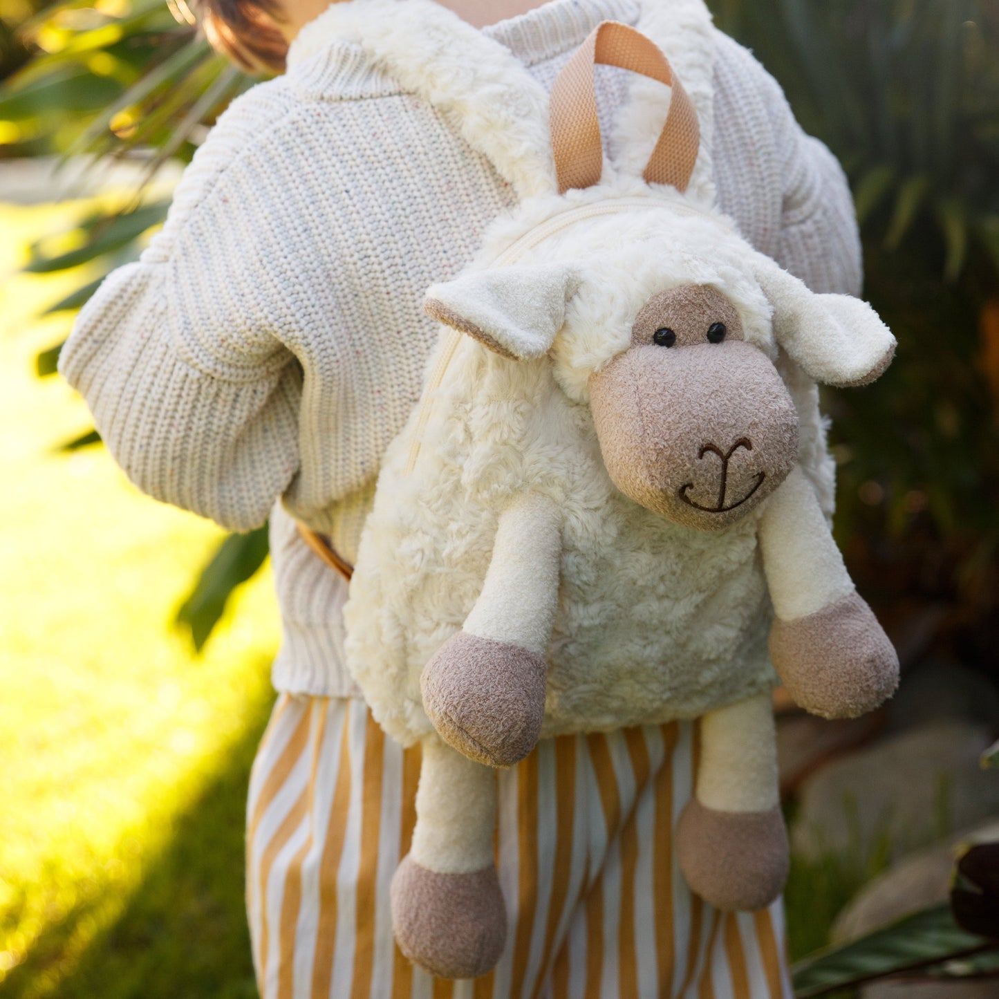 Close up of a cute fluffy whiite sheep backpack being worn outdoors by a young child.