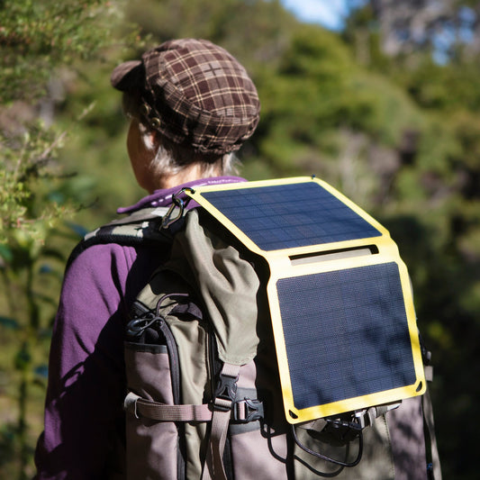 Person out hiking with a backpack and portable solar panel attached with carabiners to the pack.