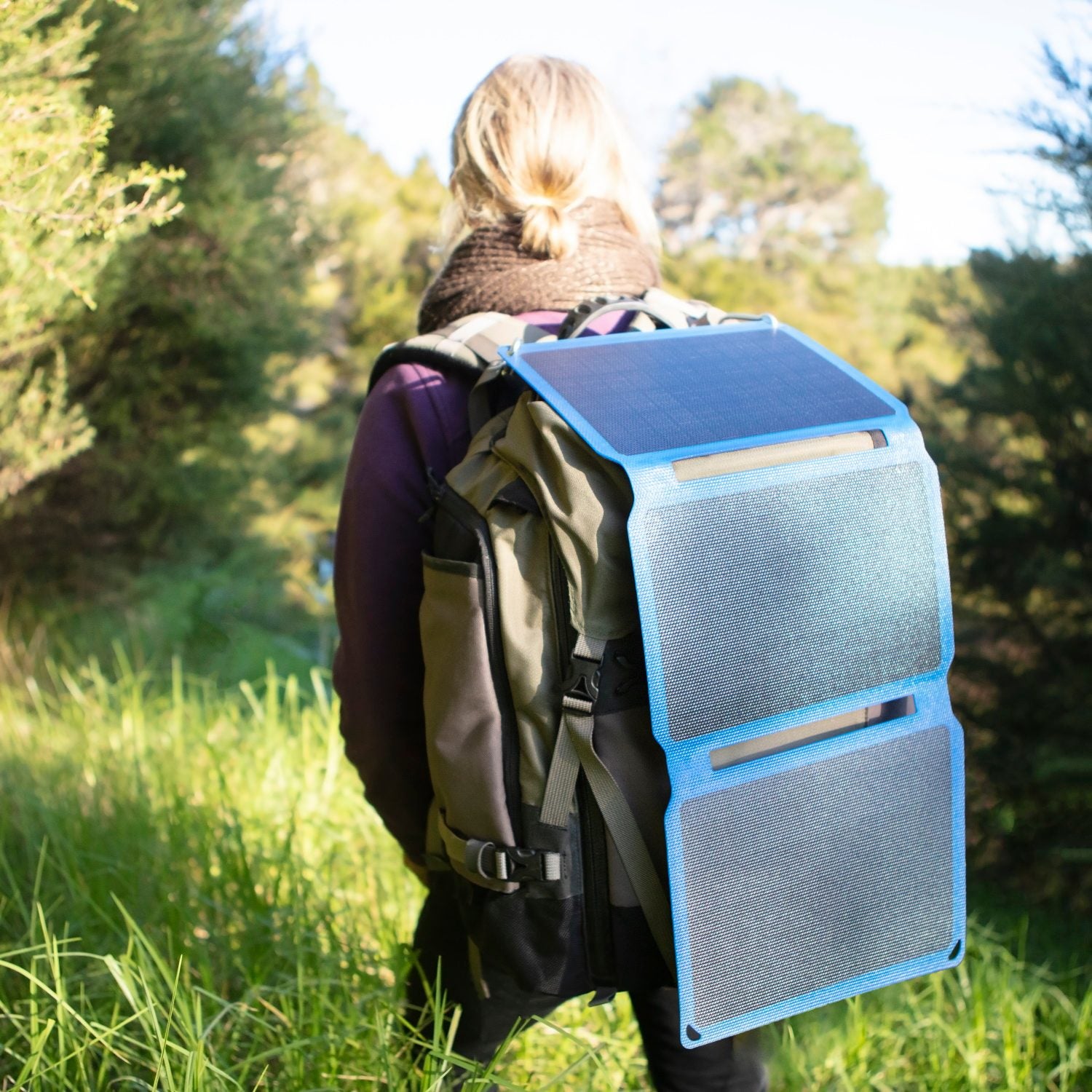 Person out hiking in the bush wearing a hiking pack and a portable solar panel attached to the pack.