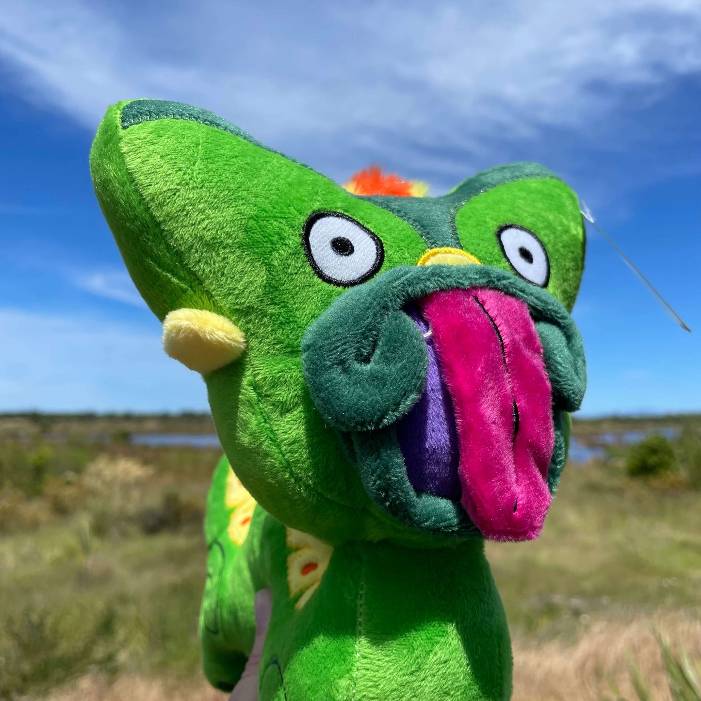 Close up of a bright green Taniwha soft toys face with big pink tongue.