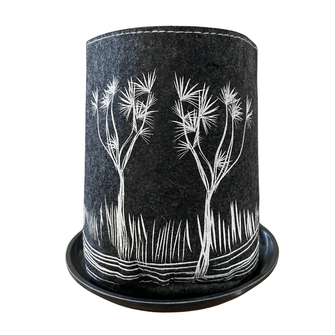 Dark grey felt plant eco plant pot with white Ti Kouka tree printed on it. sitting in a matching saucer.