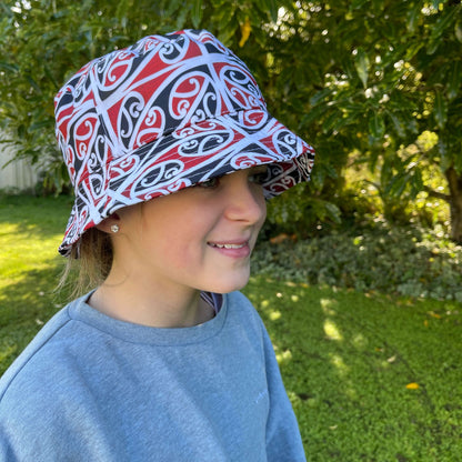 Girl wearing bucket hat with black, red & white maori koru design.