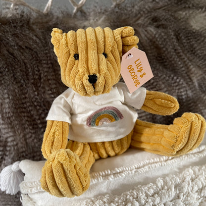 Saffron coloured teddy bear with a rainbow on his t.shirt.