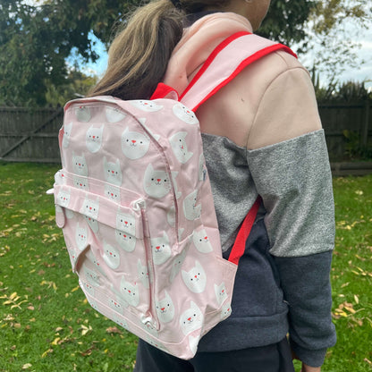 Girl wearing a pink backpack with white cat faces printed on it.