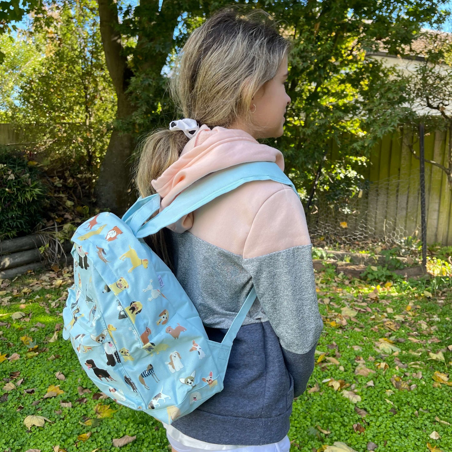 Girl wearing a pale blue backpack with various dogs printed on it.