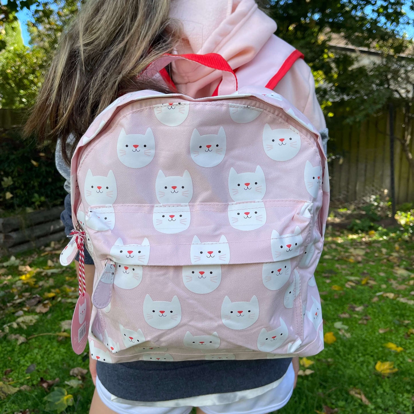 Girl wearing a pink backpack with white cat faces printed on it.