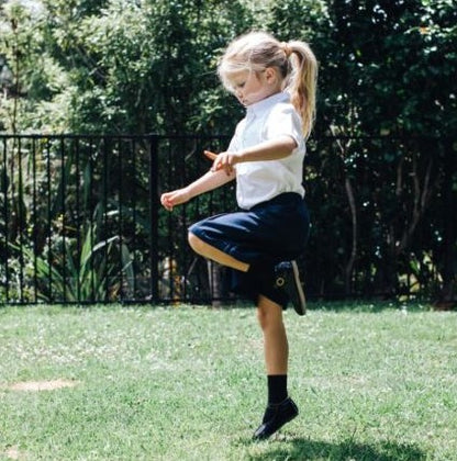 Child hopping on one foot wearing school uniform and black merino crew socks.